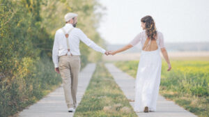 Hochzeitsfoto eines Brautpaares, die sich an den Händen halten und einen Feldweg entlang laufen