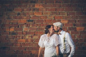 Hochzeitsfotografie eines sich küssenden Brautpaares vor einer braunen Steinwand